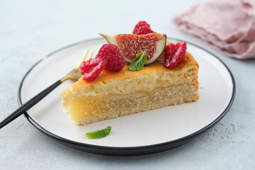 Piece of cheesecake with raspberries and figs on grey background.