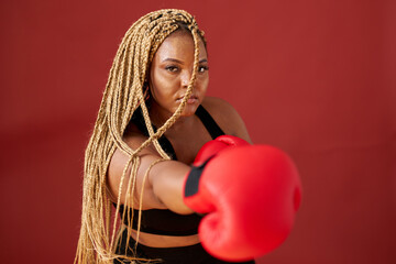 african oversize woman with red boxing mitts isolated on red background, beautiful dark-skinned female boxer training ready to fight
