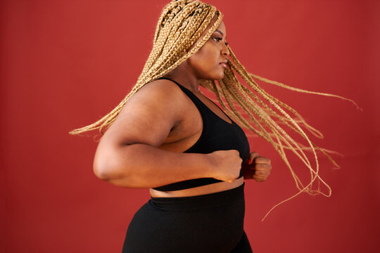 side view on african american overweight woman in action, she is doing exercises or dancing alone, wearing black sportswear. long haired female, body positive