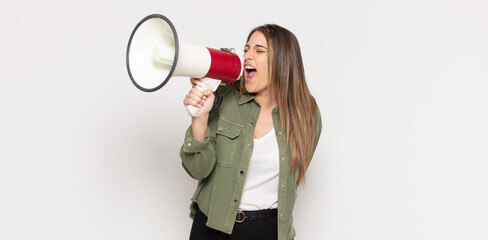 young blonde woman feeling happy, excited and positive, giving a big shout out with hands next to...