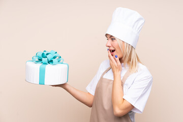 Young Russian woman with a big cake over isolated background with surprise and shocked facial...