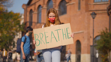 Portrait of caucasian redhead girl in mask standing outdoors with breathe cardboard sign