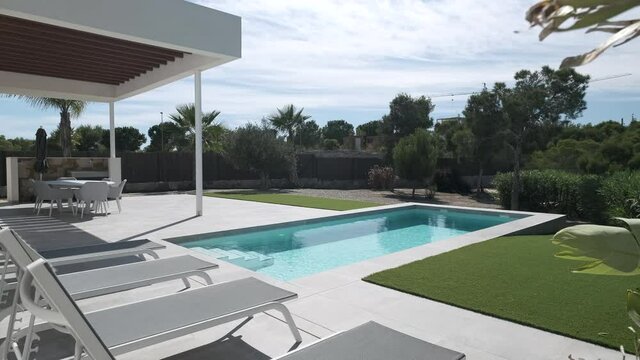 Luxury summer villa with swimming pool and empty deckchairs in row during warm summertime day. Holidays and new property, bank loan, construction industry concept. Spain