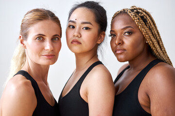 three young diverse multi ethnic female models of different race, hair colour and body size posing at camera, friendly females in black sportswear. tolerance and natural beauty concept