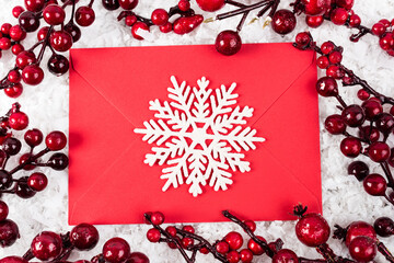 Top view of decorative snowflake on red envelope near branches with artificial berries on white textured background, new year concept