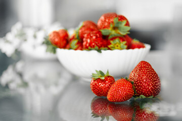 Fresh strawberries in a bowl and on a glass table, healthy food concept