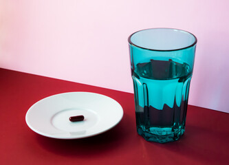 Glass of water and medical pills on a white plate on a red and pink background.