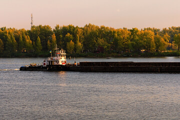 Fototapeta na wymiar Cargo delivery by river transport. The tug boat towing an empty barge. Scenic morning autumn landscape of Kyiv. Nature landscape. Dnipro River and Trukhaniv Island against cloudy sky. Kyiv, Ukraine