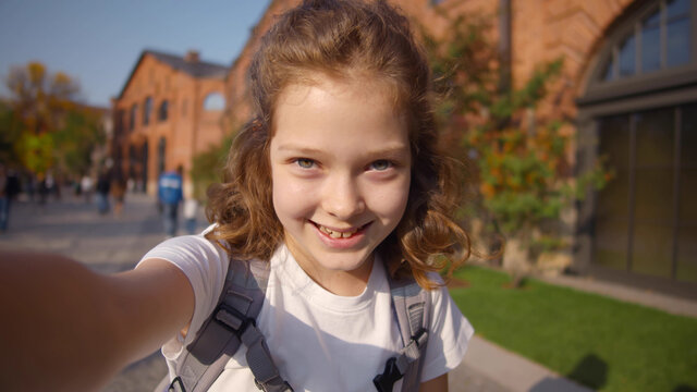 Cute schoolgirl taking selfie or having video call outside school
