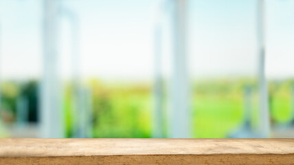 The top of the wooden table on the blur of the windowpane. Green color from a vegetable garden on the morning background. For product montage display.