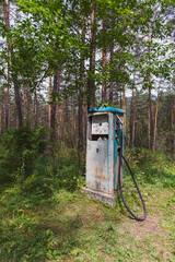 An old petrol pump for fueling a car is abandoned in a pine forest. Travel to the provinces of Russia in the summer.