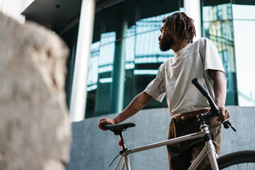 Obraz premium Handsome african american guy posing with bicycle at city street