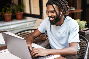 Cheerful african american guy in earphones working with laptop