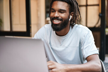 Cheerful african american guy in earphones working with laptop