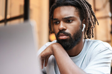 Cheerful african american guy in earphones working with laptop