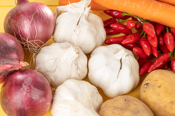 Red onions garlic potatoes carrots and red chili on a yellow wood background