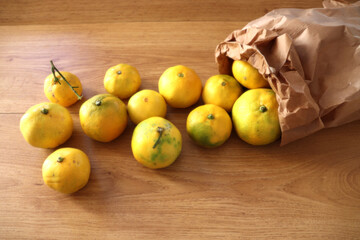 A paper bag full of mandarins and spilled mandarins on wooden background