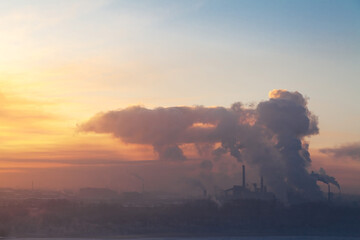 the pipes of a large plant smoke in the sky