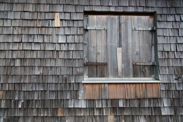 Old handcraft: Wooden and weathered shingles covering a house wall and reframing the closed wooden folding shutters