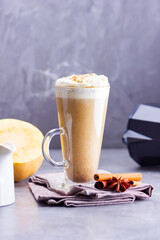 Pumpkin spice latte on a gray background. Pumpkin latte with whipped cream, coffee maker and milk jug. Hot autumn drink on cement background