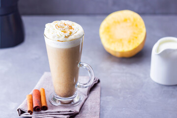 Pumpkin spice latte on a gray background. Pumpkin latte with whipped cream, coffee maker and milk jug. Hot autumn drink on cement background