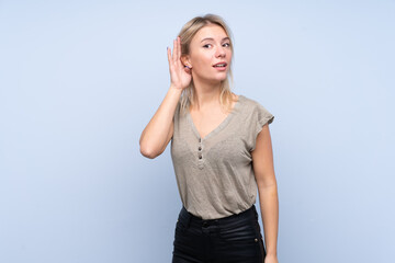 Young blonde woman over isolated blue background listening something