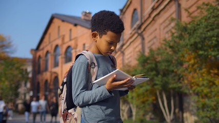 African schoolboy preparing for lesson reading book at schoolyard