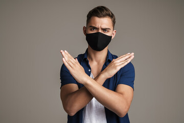 Image of caucasian displeased guy in face mask showing stop sign