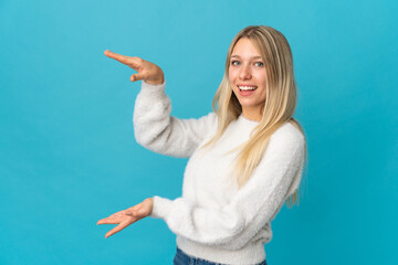 Young blonde woman isolated on blue background holding copyspace to insert an ad