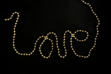 Love message written a chain of gold beads on a black background. Valentine's Day. Greeting card
