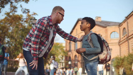 Side view of male teacher talking to preteen african schoolboy outdoors