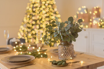 A glass of champagne in the background of the Christmas table and the lights of the Christmas tree