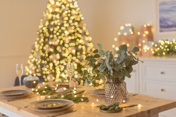 A glass of champagne in the background of the Christmas table and the lights of the Christmas tree