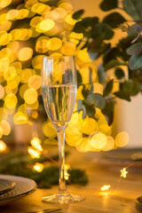 A glass of champagne in the background of the Christmas table and the lights of the Christmas tree