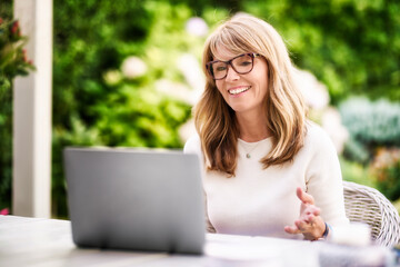 Happy mature woman having video call while sitting in the garden at home
