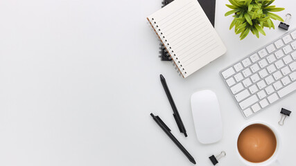 Top view white wooden workspace office desk with computer and office supplies. Flat lay work table with blank notebook, keyboard, green leaf and coffee cup. Copy space for your advertising content.