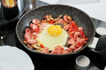 Homemade food, frying pan with scrambled eggs and paprika sausages on hob
