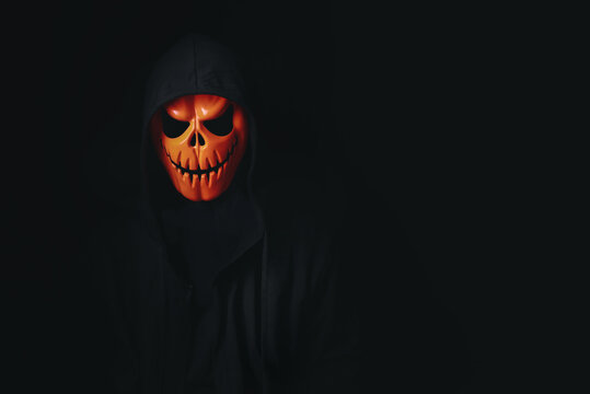 man in spooky pumpkin skull cosplay in black dressed for halloween festival on black background