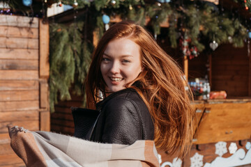 Winter outdoor portrait of a red-haired woman in natural tones. Young woman enjoying life on street Christmas Fair