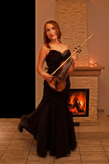 happy young violinist stands in a long black dress, near the fireplace, vertical