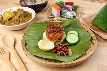 Nasi Lemak fragrant rice coconut milk with sambal friend peanut anchovy egg packed banana leaf round bamboo plate colorful nyonya kuih sweet desert palm leaf plate on wooden background