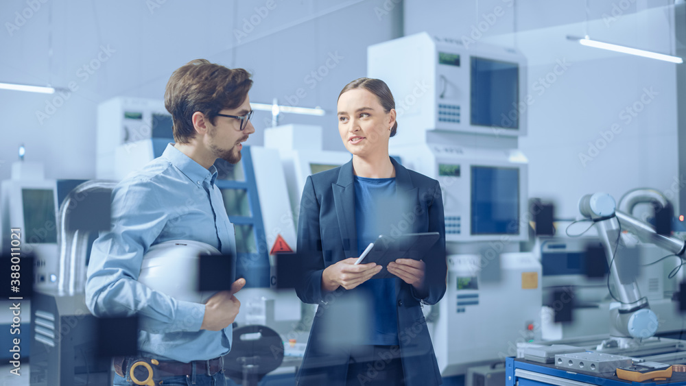 Poster Modern Factory: Female Project Manager and Male Engineer Standing, Talking, Using Digital Tablet for Programming and Monitoring Assembly Line. Industry 4.0 Facility with High Tech Machinery