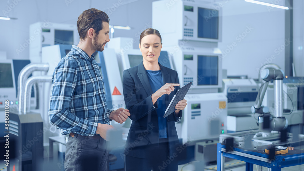 Poster Modern Factory: Female Project Manager and Male Engineer Standing, Talking, Using Digital Tablet for Programming and Monitoring Assembly Line. Industry 4.0 Facility with High-Tech CNC Machinery