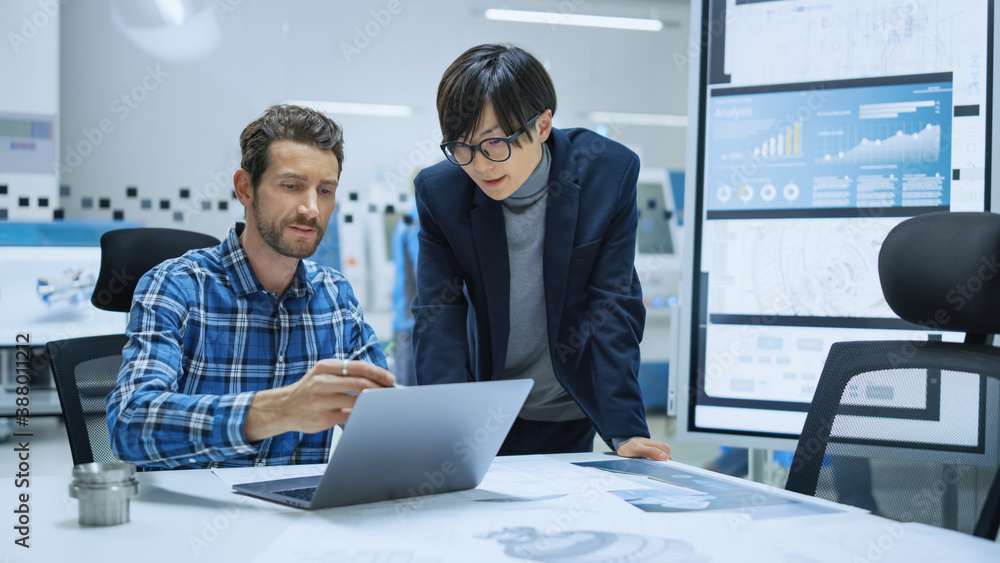 Poster modern factory: industrial engineer sitting at his desk, working on laptop computer, talks with chie
