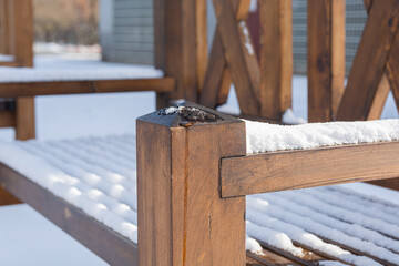 A brown wooden bench in a city park is covered with snow