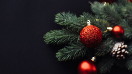 Red Christmas balls on a branch of a Christmas tree on a black background. Greeting card template, web banner mockup. Flat lay, top view, copy space