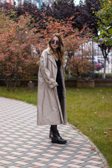 attractive slim young brunette in fashionable trench, black dress and sunglasses in park. autumn, yellow leaves.