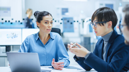 Modern Factory Office Meeting Room: Multi Ethnic and Diverse Team of Engineers, Managers and Investors Talking Sitting at Conference Table, Analyzing Computer Printed Circuit Board Element