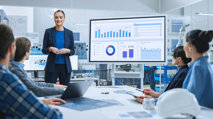Modern Industrial Factory Meeting: Confident Female Engineer Uses Interactive Whiteboard, Makes...