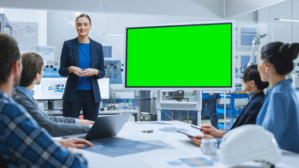 Modern Industrial Factory Meeting: Confident Female Engineer Uses Interactive Green Mock-up Screen Whiteboard, Makes Report to a Group of Engineers, Managers 